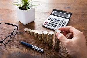 A hand calculating stack of coins on a Wooden Desk.Retirement Plan Consulting eases in Choosing the right Plans